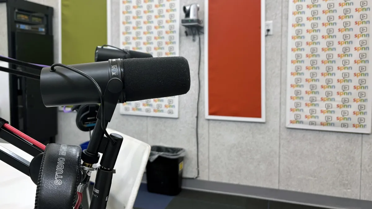Two microphones on boom arms over a table in a small podcast recording studio