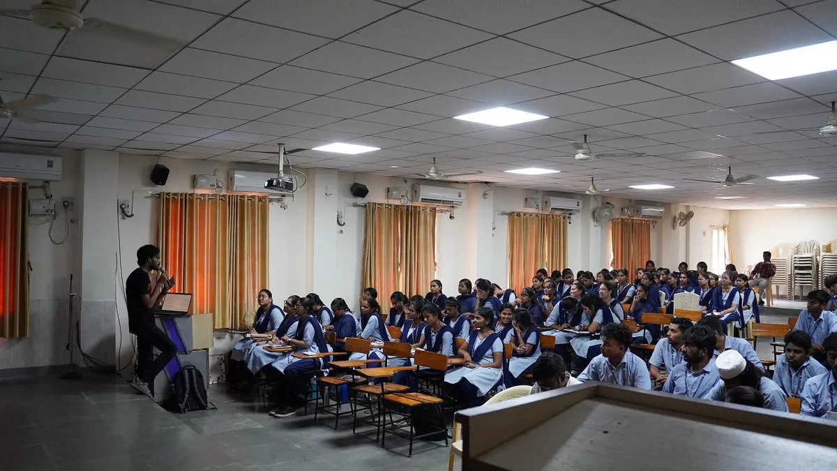 A training room with rows of chairs facing a projector screen and a speaker at the front