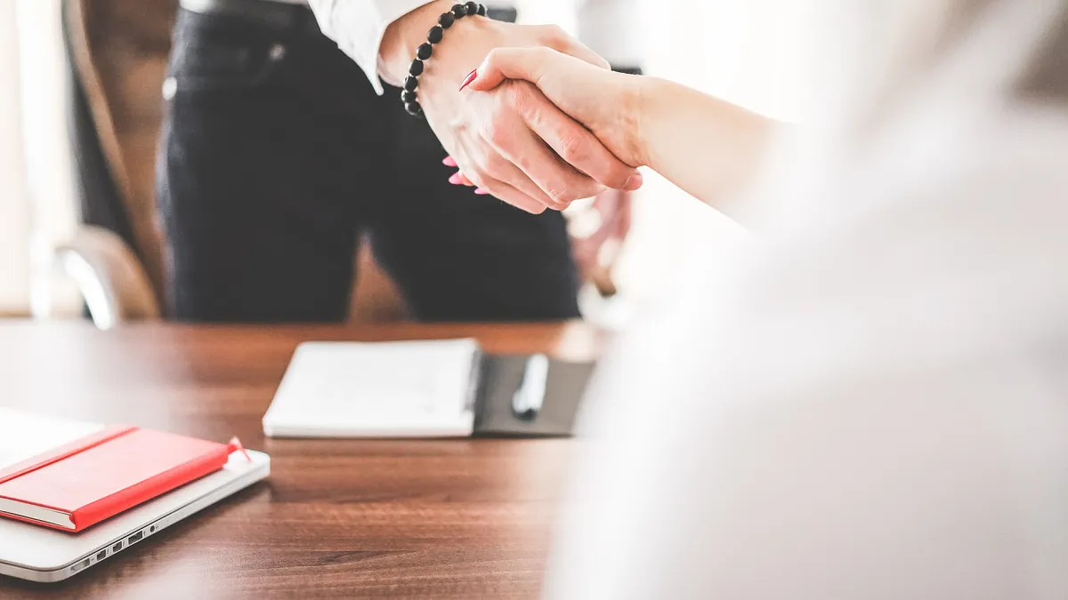 Hands signing a printed agreement on an office desk next to a pen and folder