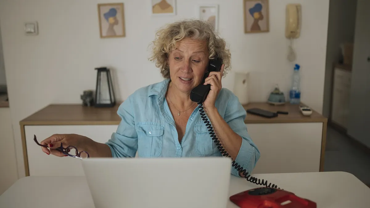 A person on a video call on a laptop at a shared desk with headphones on