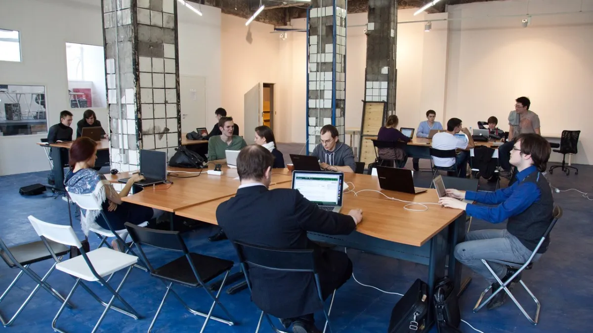 Rows of shared desks with laptops and office chairs in a bright coworking space