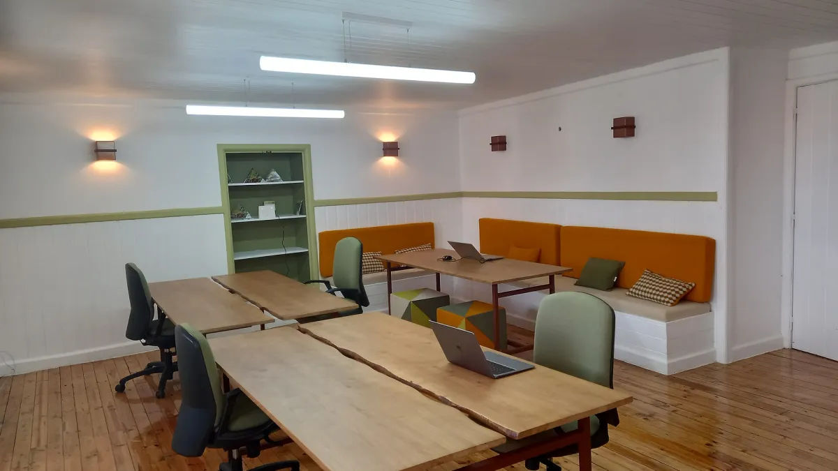 An open laptop on a shared desk in a coworking space with other people working nearby